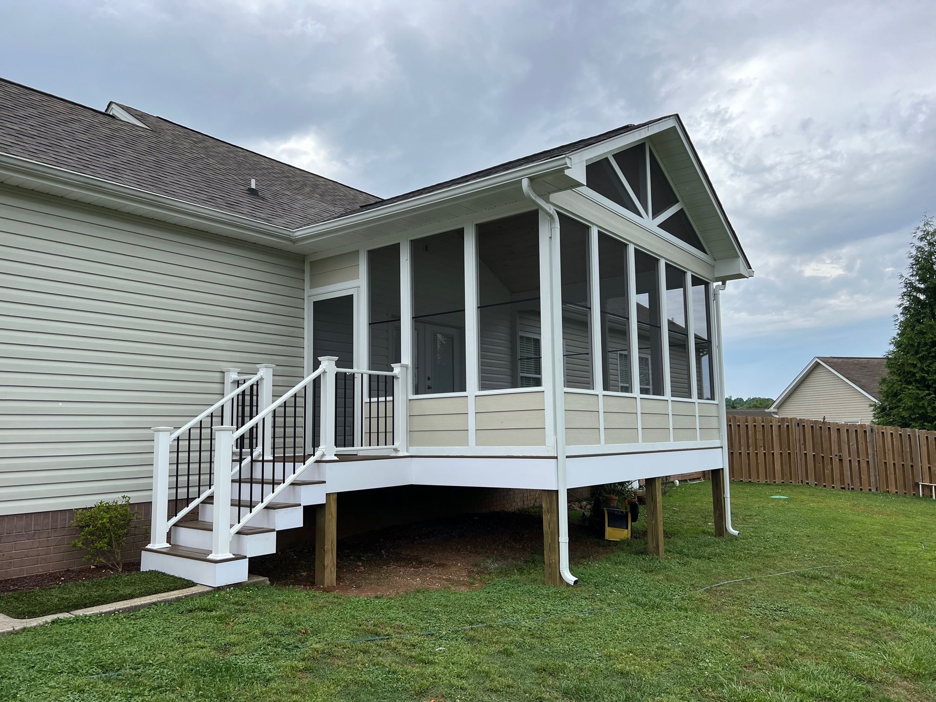 A screened in porch with stairs is in the backyard of a house.