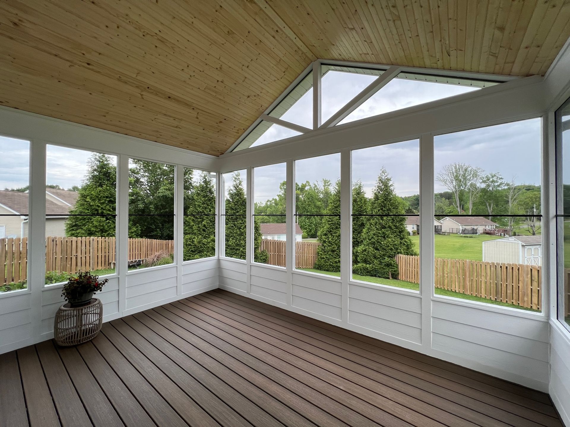 A screened in porch with a wooden deck and lots of windows.