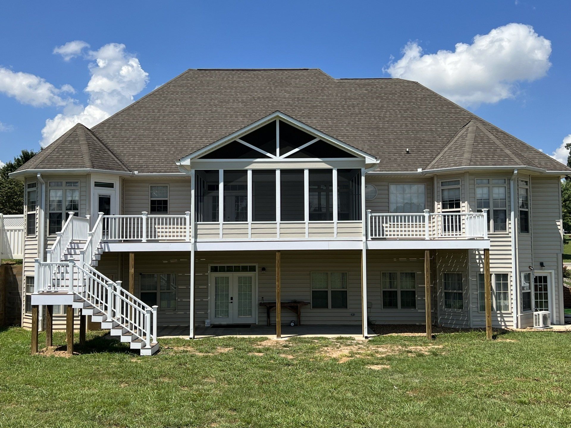 The back of a large house with a screened in porch and stairs.