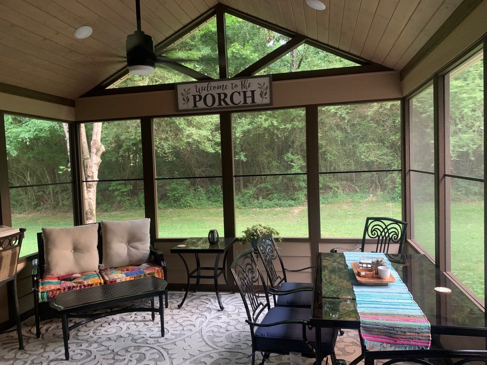 A screened in porch with furniture and a sign that says welcome to the porch.