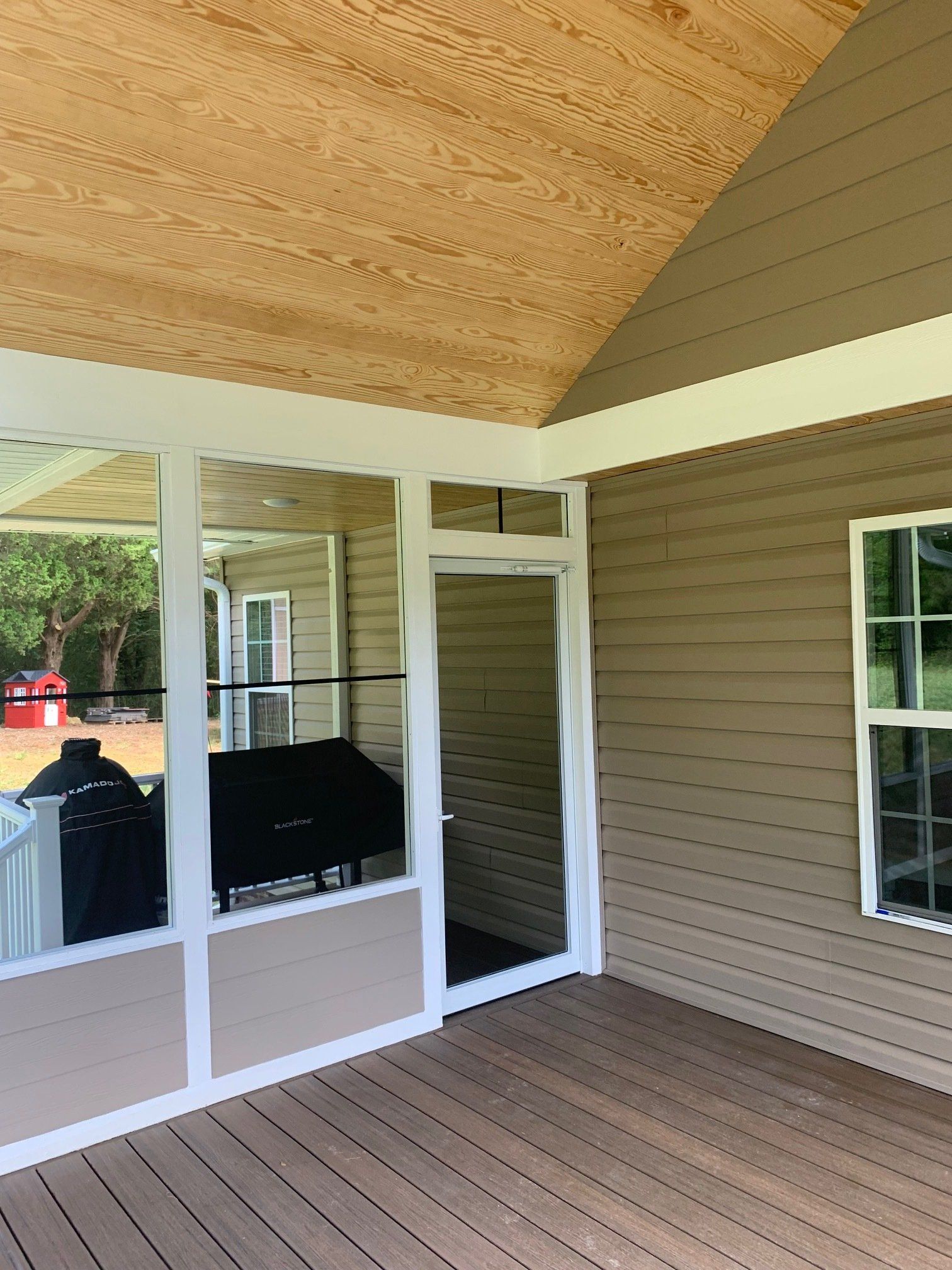 A screened in porch with a wooden deck and a grill.