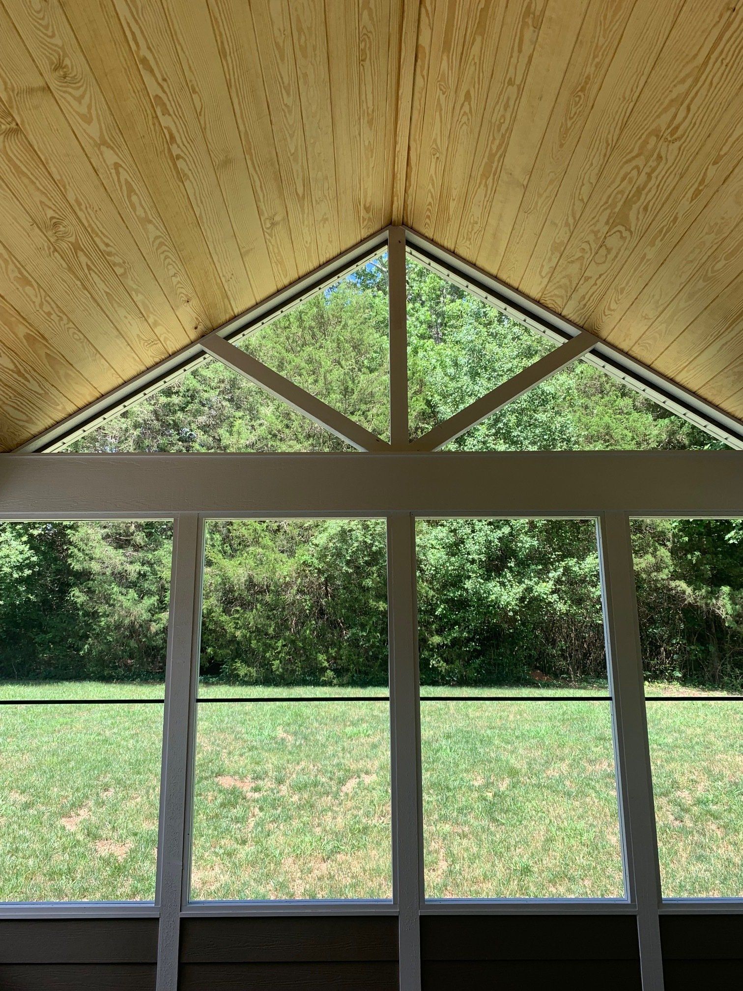 A screened in porch with a vaulted ceiling and a view of a lush green field.