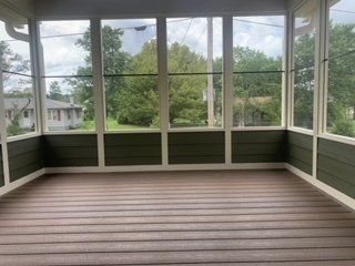 An empty screened in porch with a wooden floor and lots of windows.