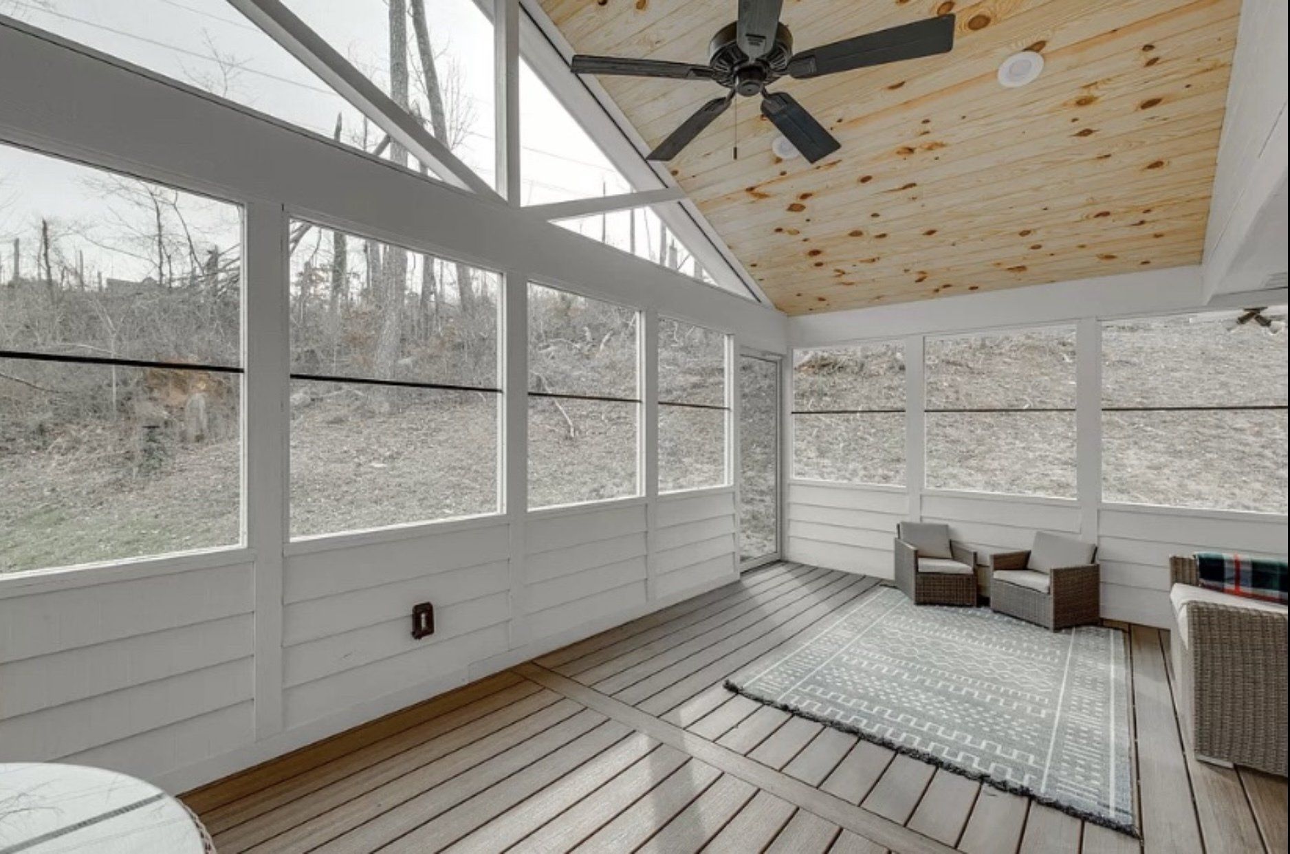 A screened in porch with a ceiling fan and lots of windows.