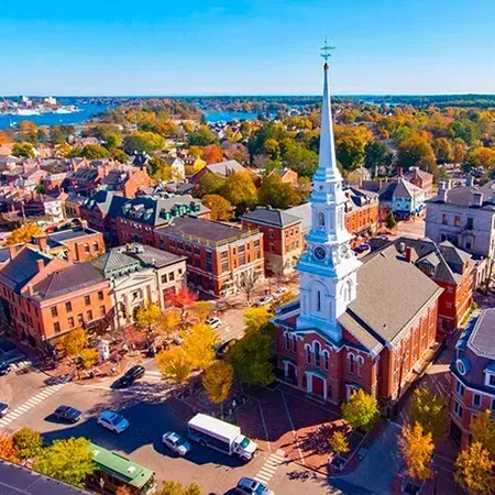 Aerial view of Portland, Maine, with church steeple dominating the town center, surrounded by buildings and colorful autumn trees.