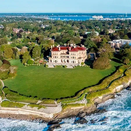Aerial view of a large mansion on a grassy lawn next to ocean waves.