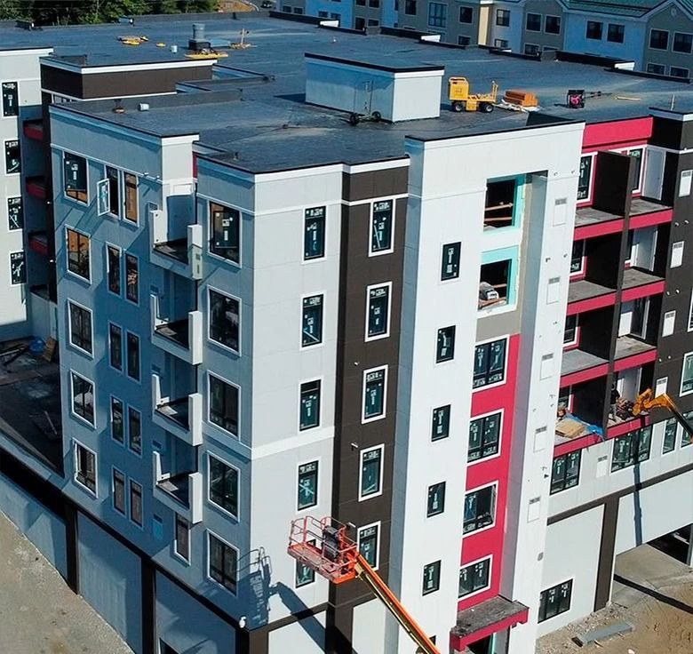 Multi-story apartment building under construction, featuring gray, white, red, and brown facades; aerial view.