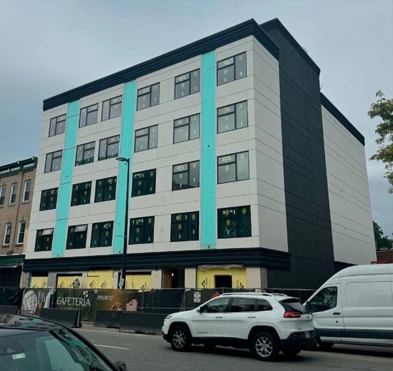 Multi-story building under construction with white and teal accents; cars in front.