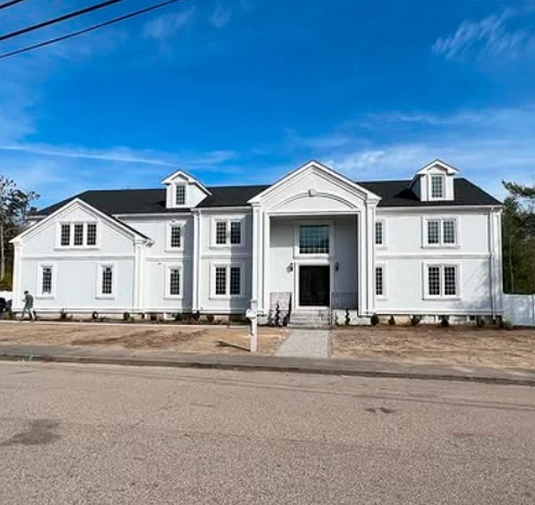 Large, two-story light gray house with black roof, white trim, and a blue sky background.