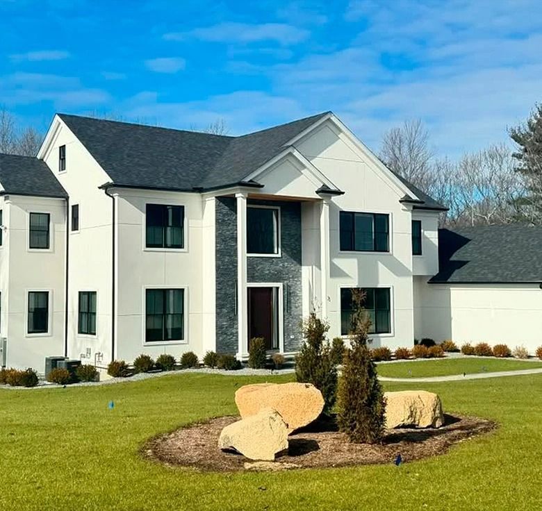 Modern white house with dark trim, gray stone accent, green lawn, blue sky.