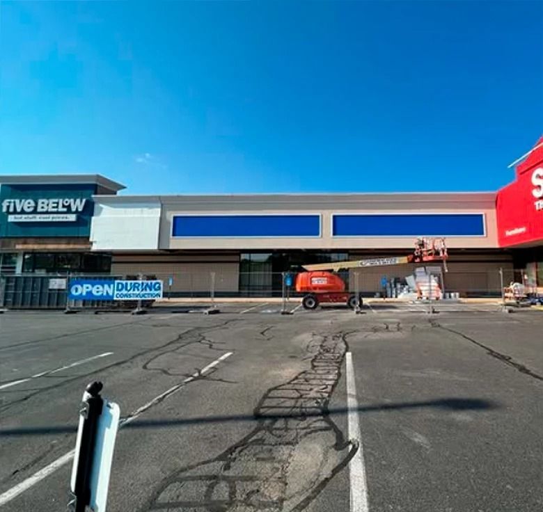Exterior of a strip mall with a Five Below store and a blank storefront under construction, blue sky.
