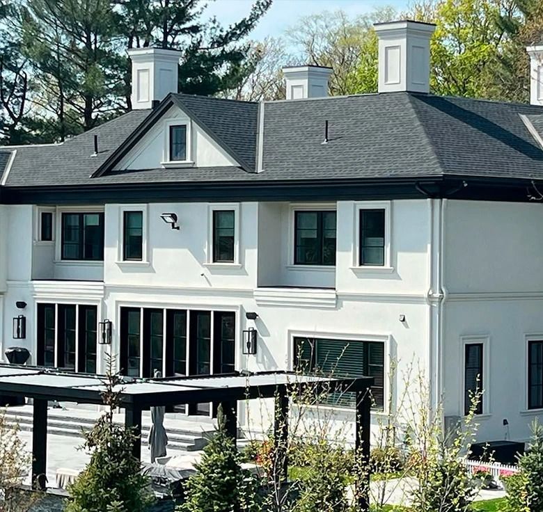 White two-story house with black trim, windows, and roof. Chimneys and a pergola are also visible.
