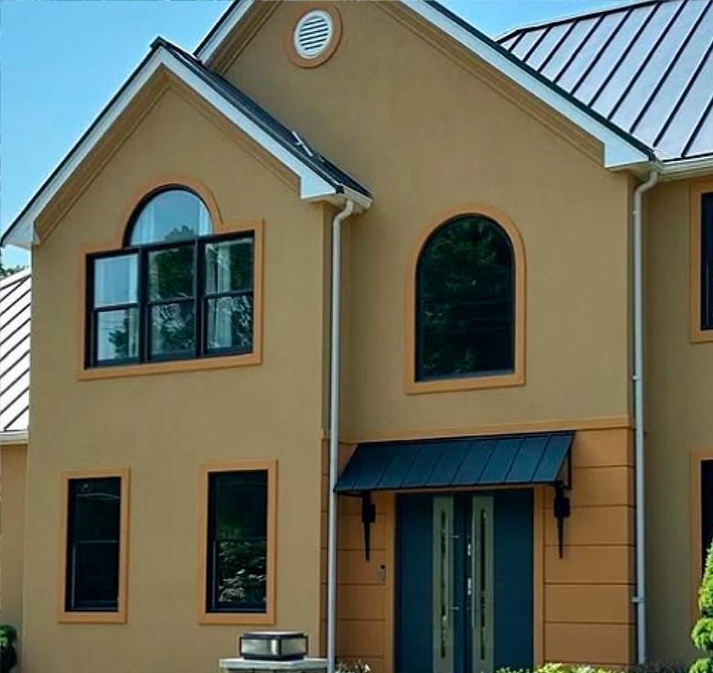 Tan stucco house with black-framed windows, teal door, and a black awning under a blue sky.