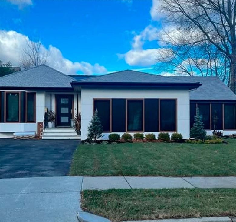 Modern white house with dark trim and windows, dark roof, blue sky, green grass.