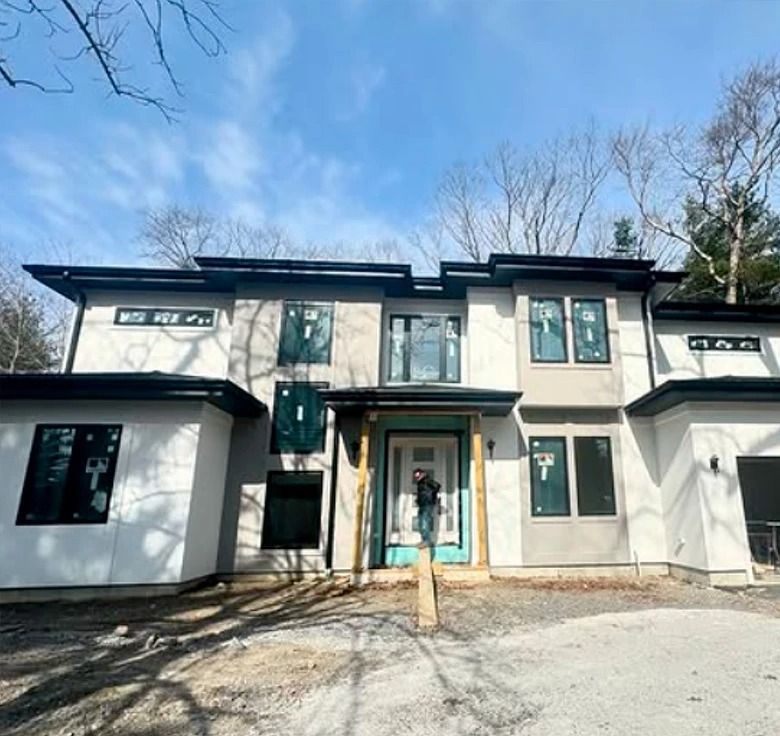 Modern two-story house with gray and white stucco exterior, black trim, and a blue front door; construction in progress.
