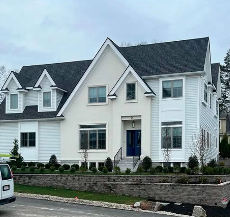 Two-story house with a white stucco facade and light blue siding, black roof, and manicured landscaping.