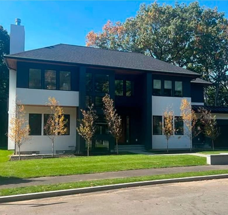 Two-story modern house with black and white exterior, green lawn, trees, and blue sky.