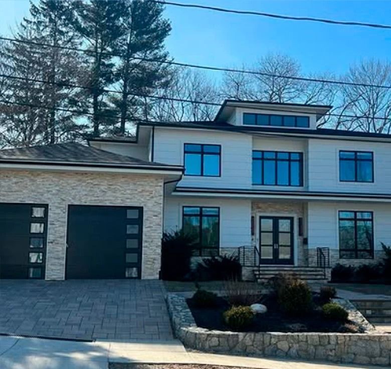 Modern two-story house with light facade, dark garage doors, and stone accents on a sunny day.