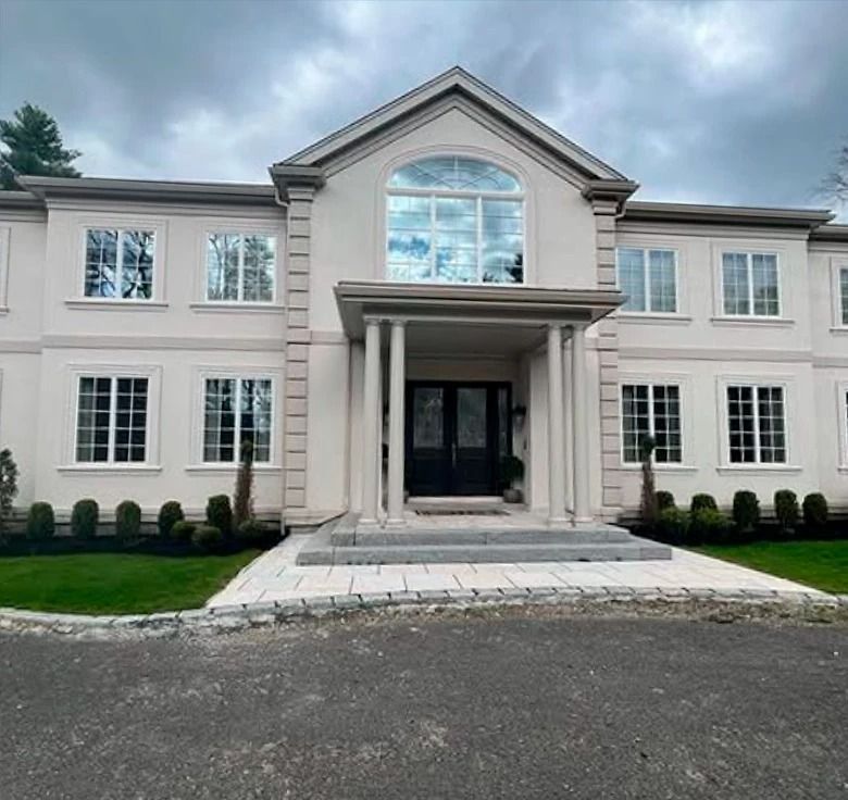 Exterior of a large, pale stucco house with multiple windows and a columned entrance under a curved window.