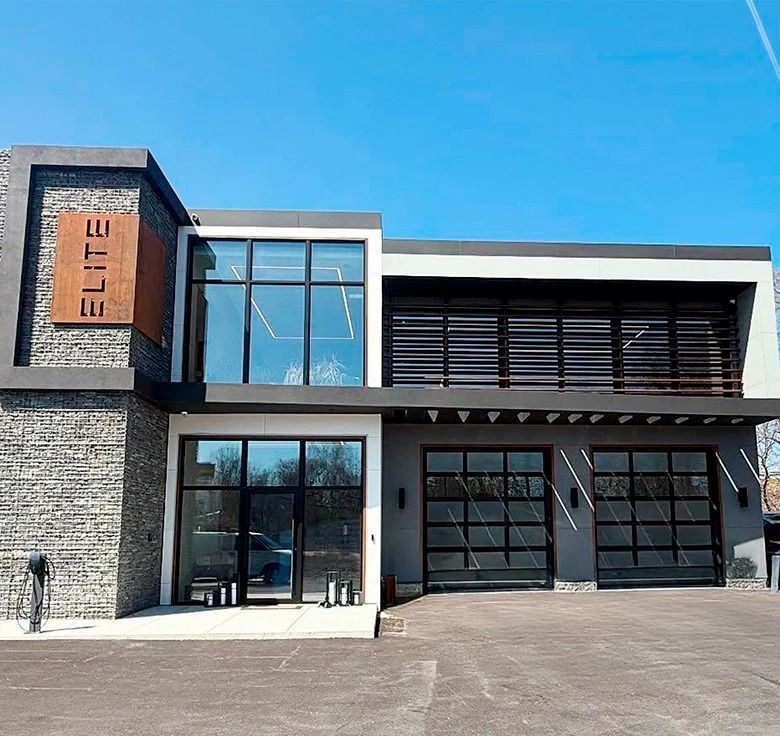 Modern building with gray and stone facade, large windows, and garage doors. 