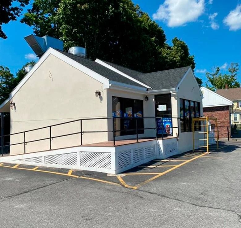 Cream-colored building with a ramp and black railing. A small business with a black roof and large windows.