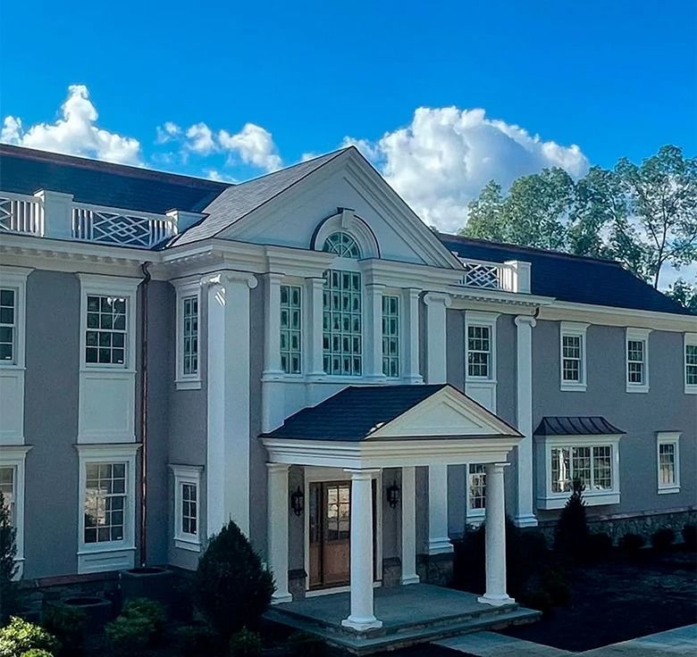 Large gray house with white columns, a dark roof, and blue sky.