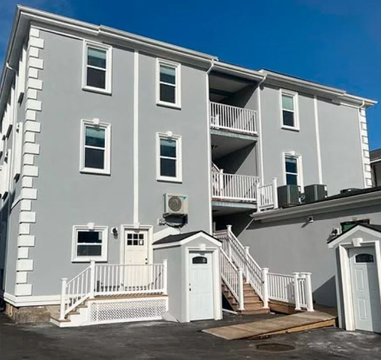 Multi-story gray building with white trim, windows, balconies, stairs, and a ramp.