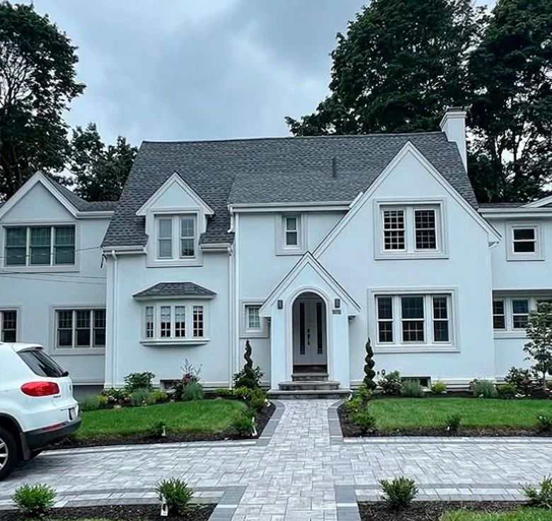 White two-story house with gray roof, brick walkway, and green lawn. SUV parked on the left.