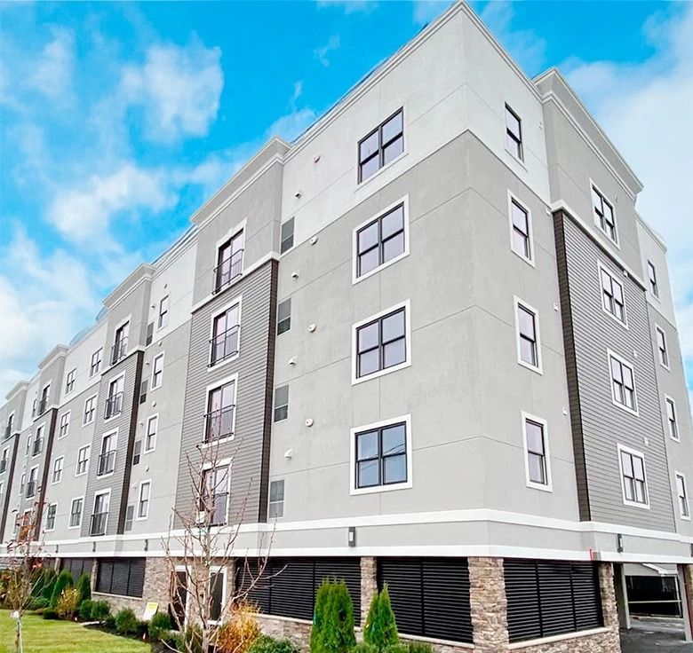 Multi-story modern apartment building with gray and white facade under a blue sky.