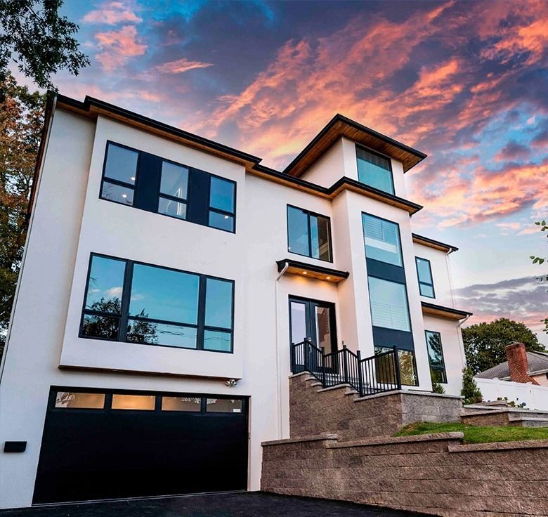 Modern white house with dark framed windows, black garage door, and a sunset sky.