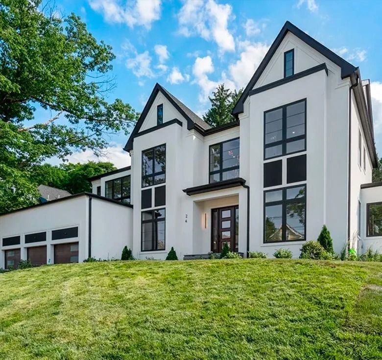 White modern house with black trim, large windows, and a grassy hill in front.