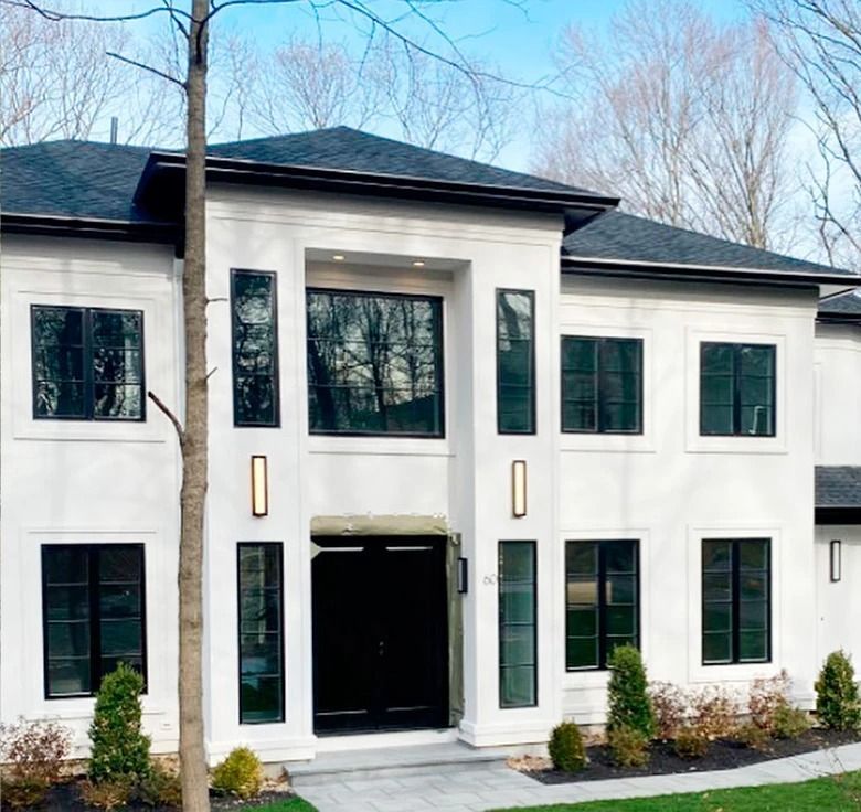 White stucco house with dark trim and windows. Black front door, landscaping, and a blue sky.