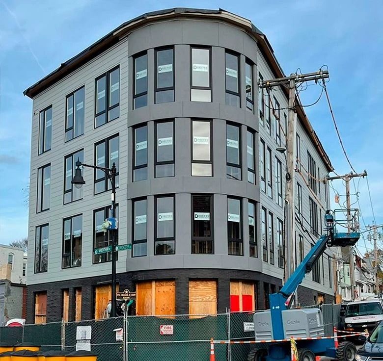 A multi-story gray building under construction with boarded-up windows and a blue lift.