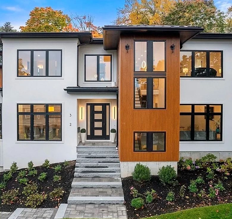 Modern white house with black-framed windows, wood accents, and gray steps leading to the front door.