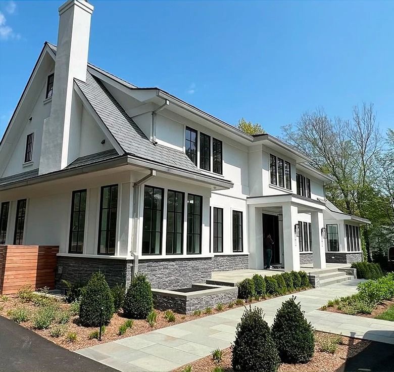 White two-story house with gray roof and stone accents, blue sky background.
