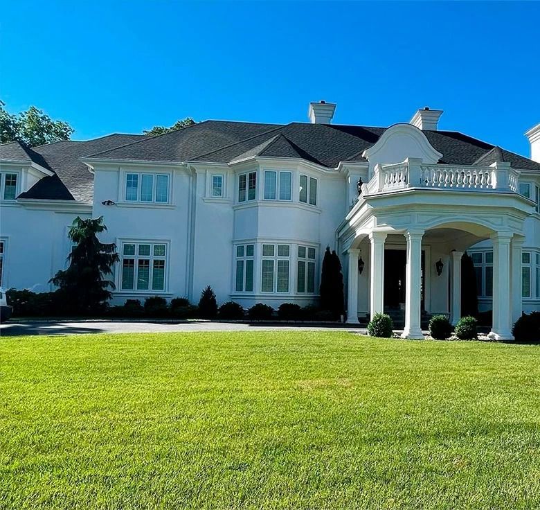 White mansion with a green lawn under a clear blue sky.