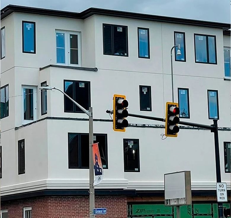 Building with black-framed windows, traffic lights, and a brick base. Gray sky.