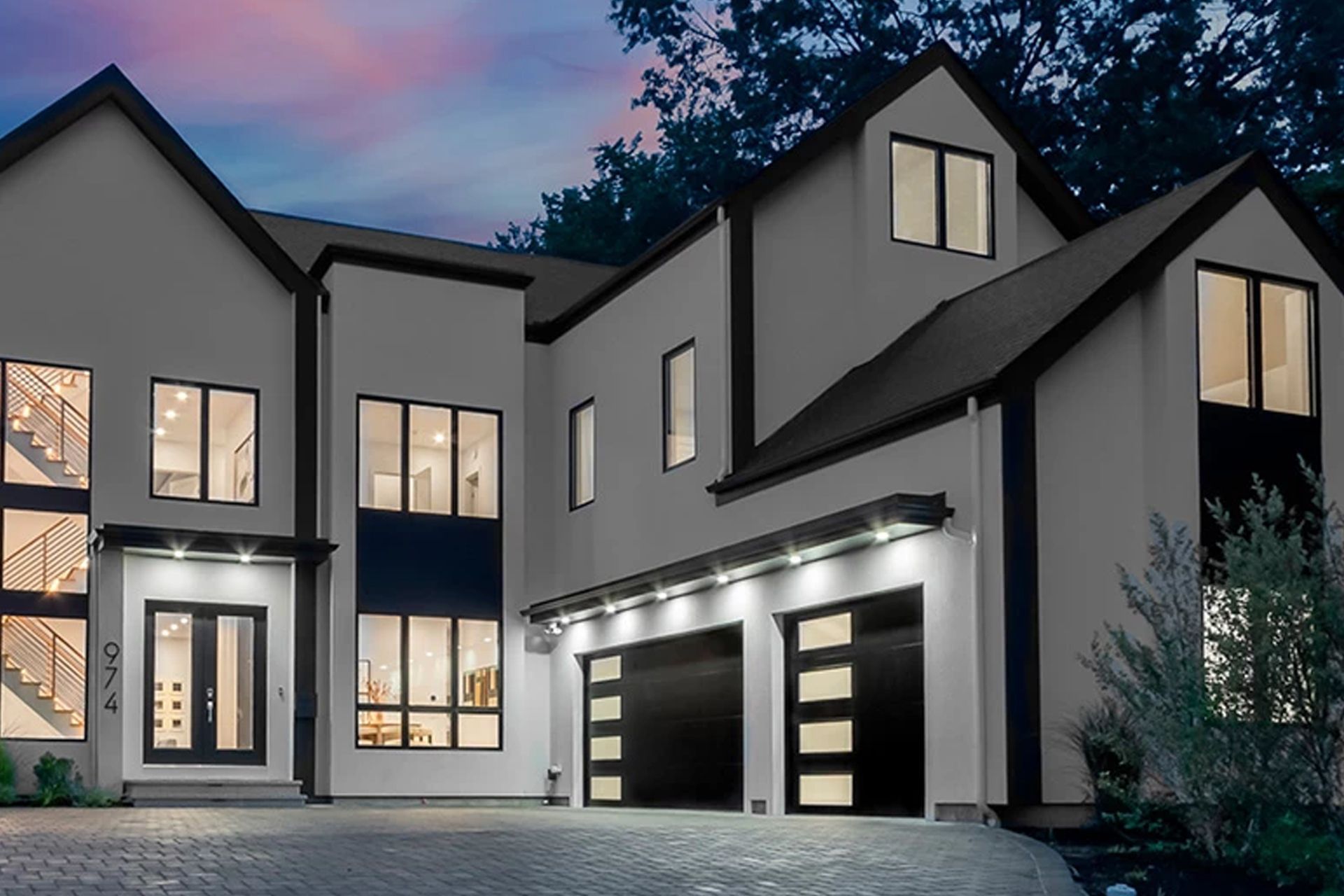 Modern two-story house with dark trim and garage doors, featuring multiple windows, and exterior lighting.