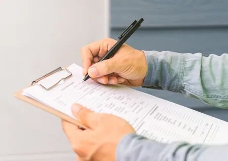 Person holding a clipboard and pen, writing on a form.