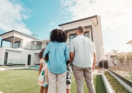 Family looking at a modern white house with a green lawn under a sunny sky.