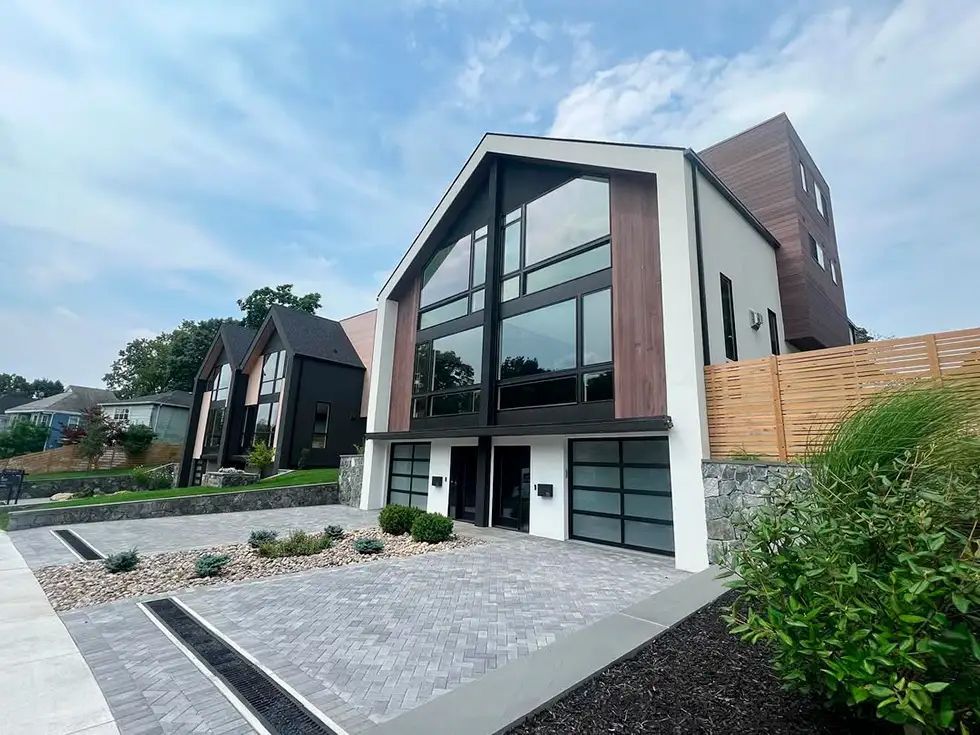 Modern two-story house with large windows, brown siding, and gray driveway under a blue sky.