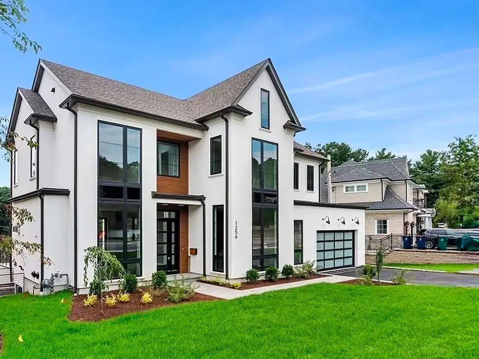 Modern white house with black-framed windows, green lawn, and a garage. Clear blue sky.