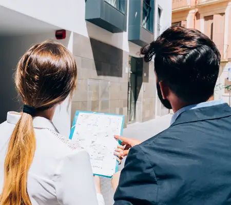 Woman and man looking at a map on a clipboard outdoors. They are in a city alleyway.