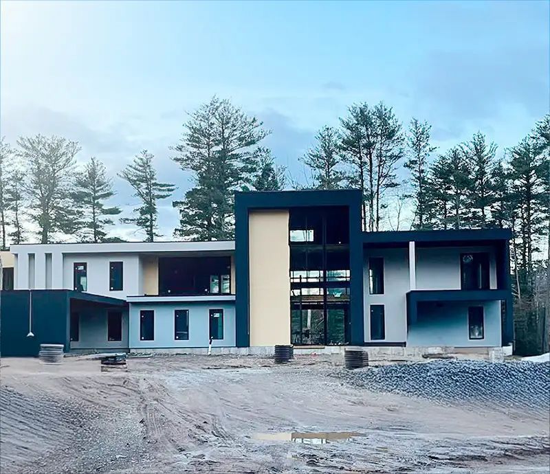 Modern house under construction with a black and beige facade, set against a backdrop of trees.