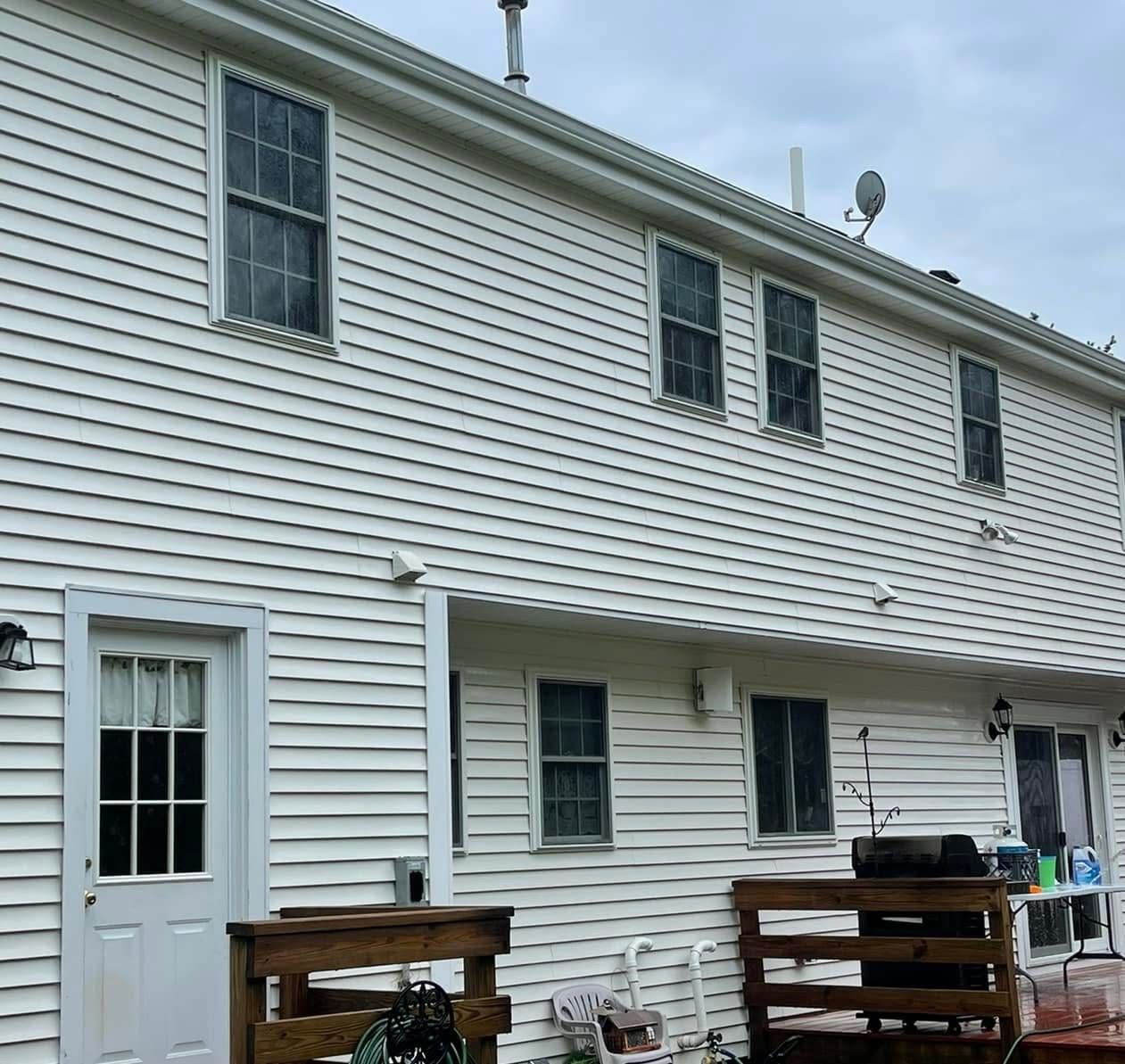 A two-story house with white horizontal siding and a wood deck at ground level.