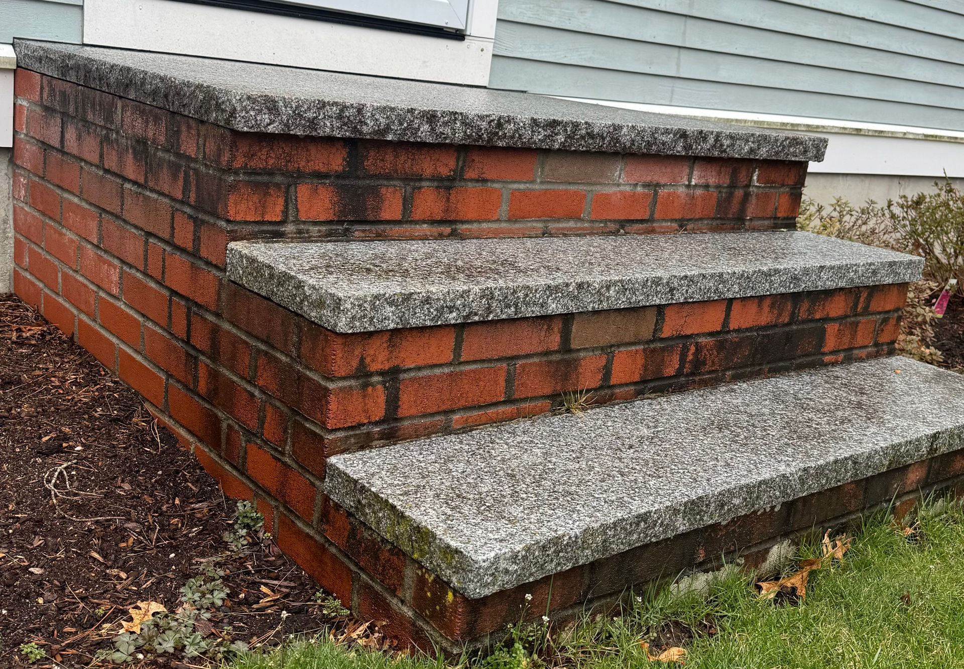 Three brick steps leading to a house entrance, featuring gray speckled stone treads.