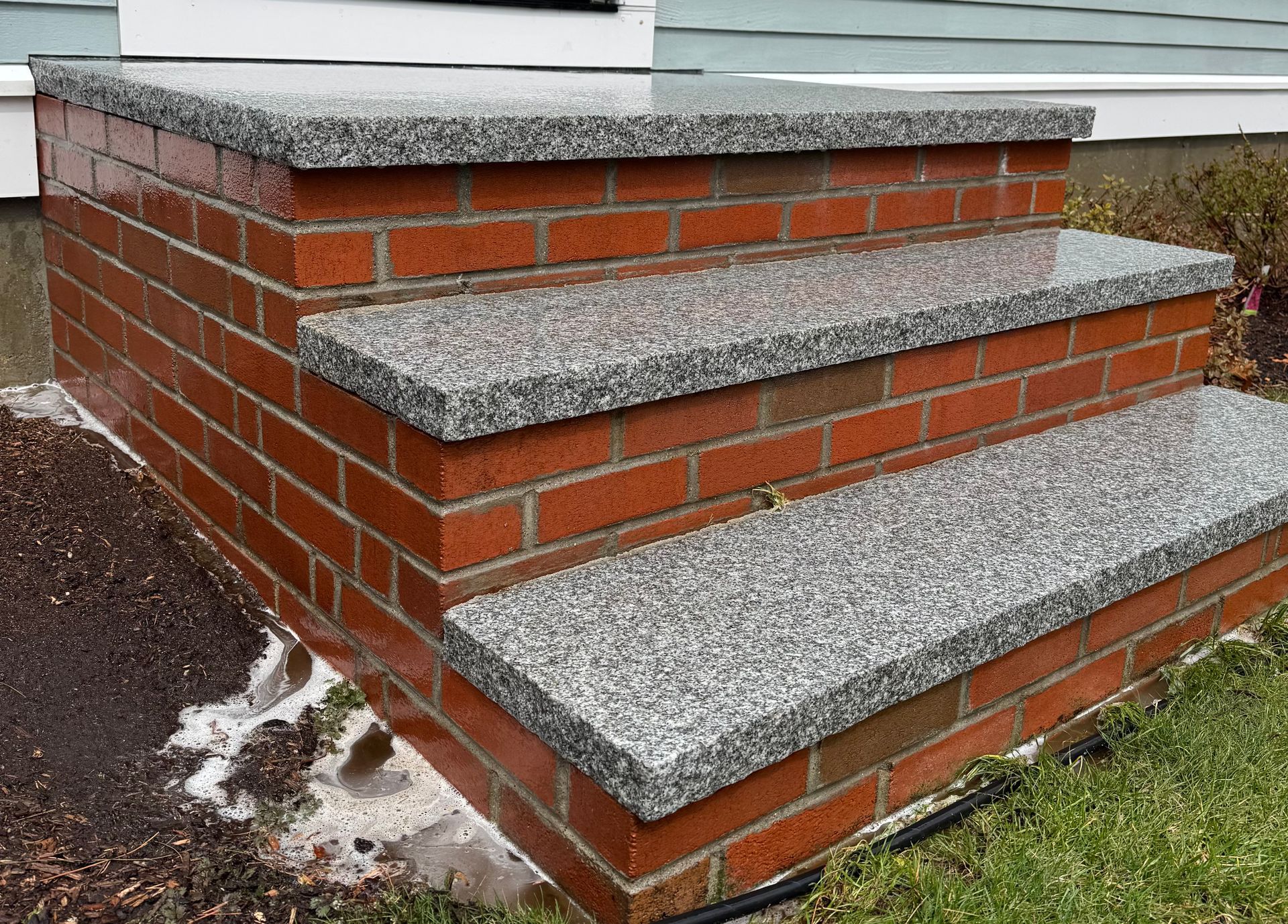 Three brick steps leading to a house entrance, featuring gray speckled granite treads and a matching top landing.