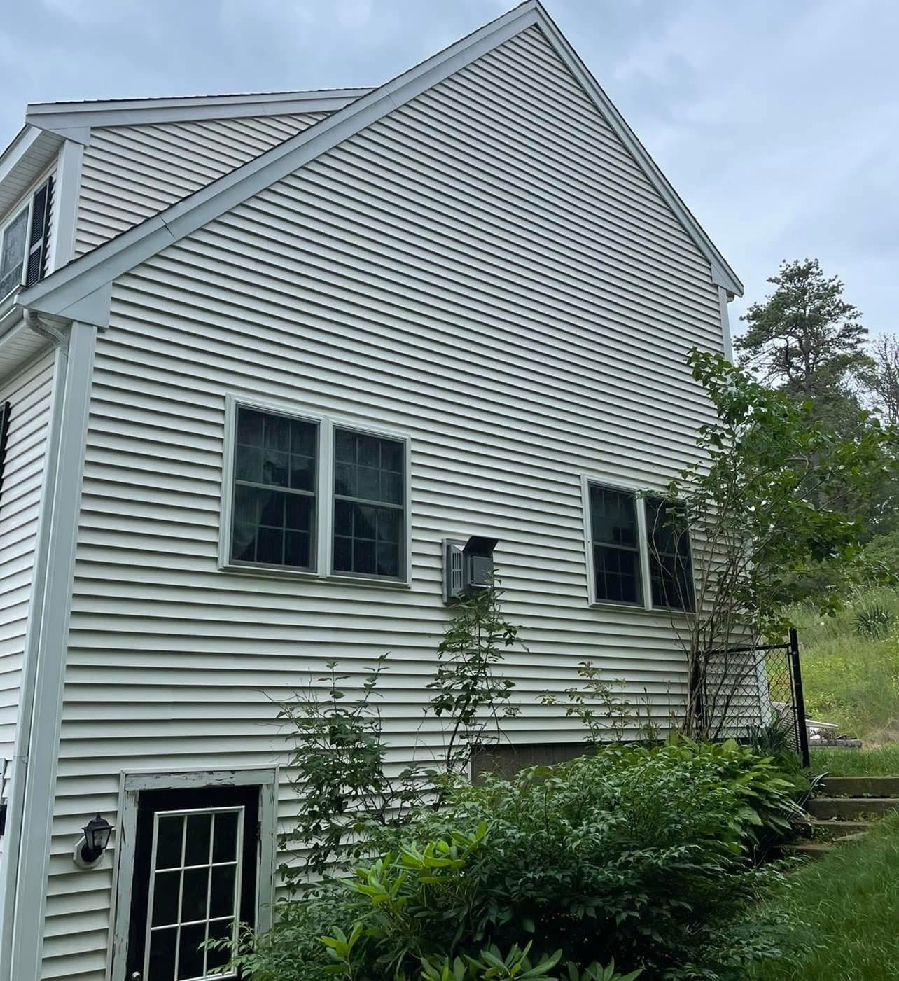 Side view of a two-story house with white vinyl siding, black-framed windows, and a dark-framed basement door.