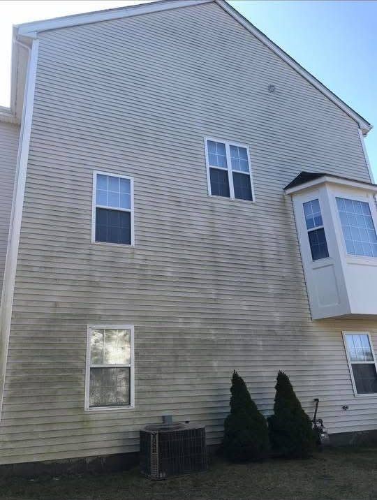 A light-colored house exterior with stained, dirty siding and a bay window, showing areas in need of cleaning.