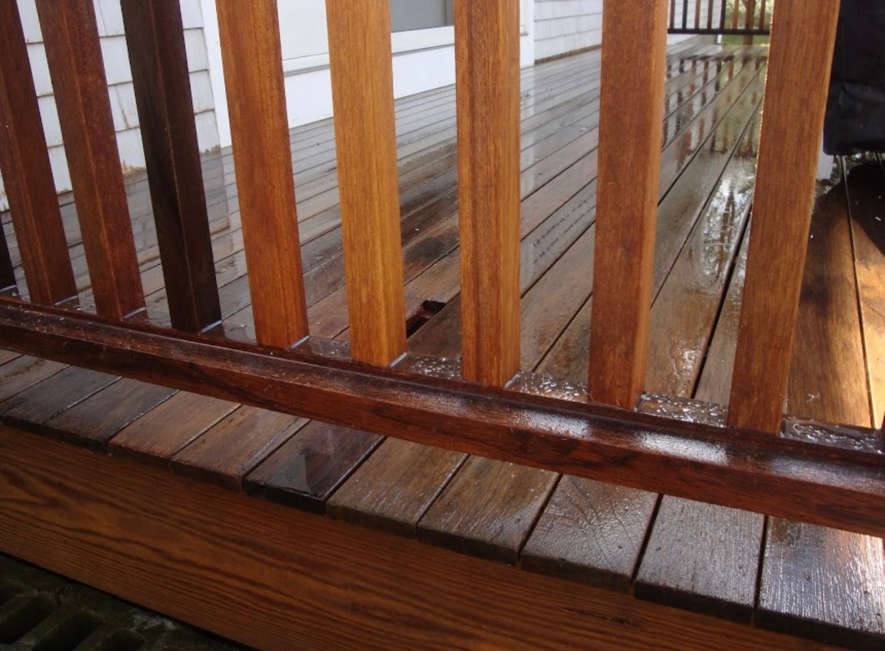 A close-up view of a wet wooden deck with vertical railing spindles and a horizontal handrail.